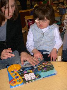 A girl with glasses looks at a tactile book with her teacher