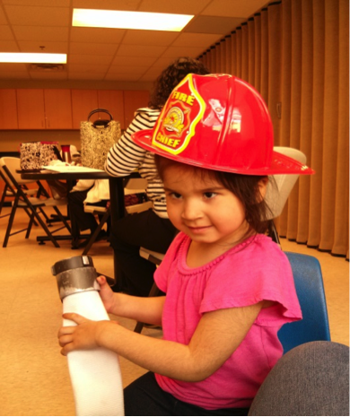 A young girl wearing a fire chief hat and holding a fire hose