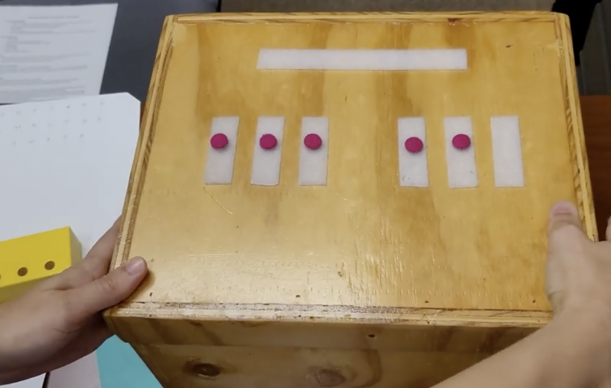 Two hands on the edges of a Braille Box