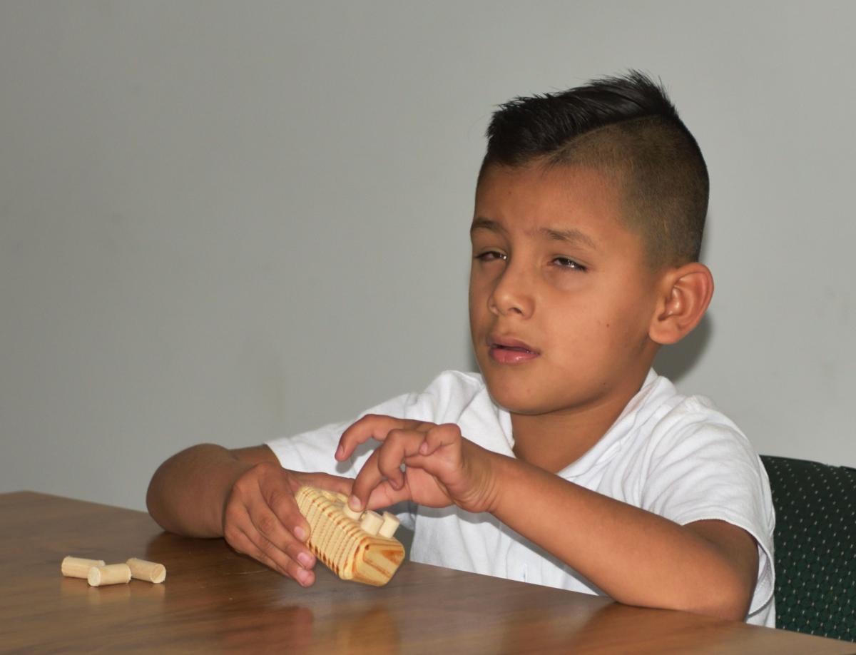 A boy places wooden pegs in a wooden frame.