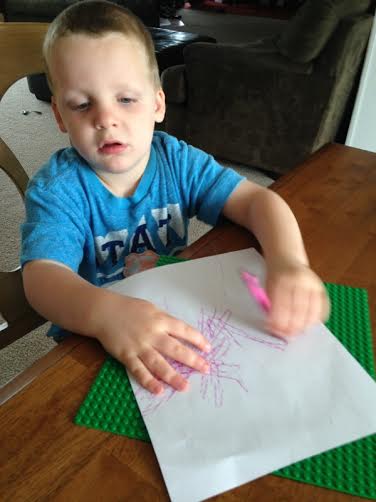 child scribbling on paper over a raised surface
