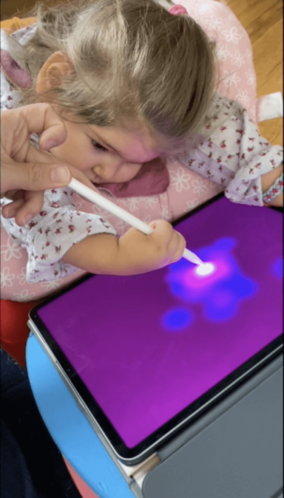 A young girl holds a stylus on an iPad while her teacher holds on above her hand