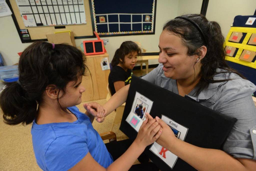 A teacher uses tactile sign language with a young girl