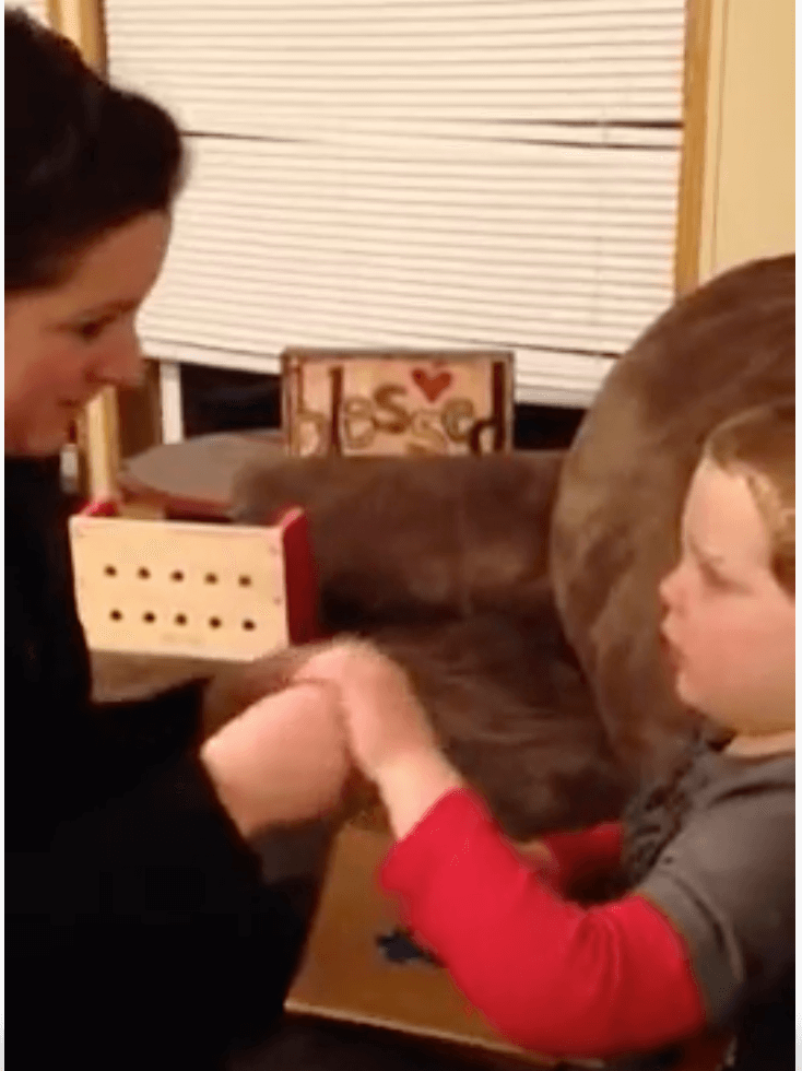 A mother uses tactile sign language while reading a book with her young son who is deafblind.