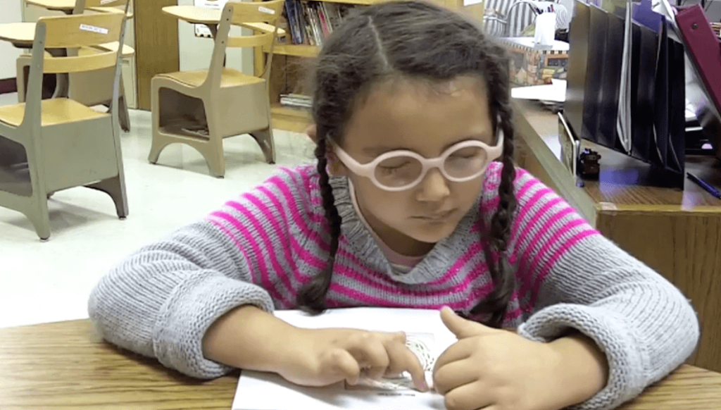 A girl with glasses examines a tactile worksheet.