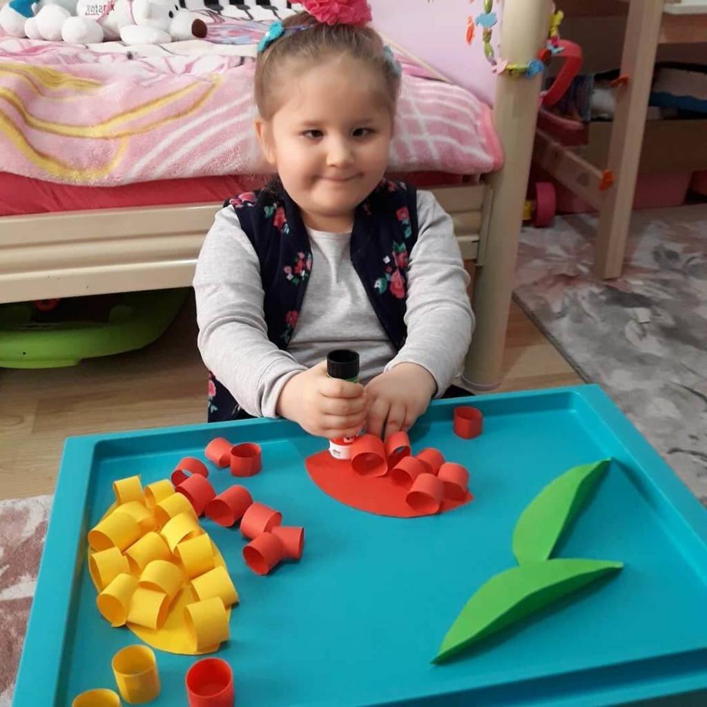 A young girl uses a glue stick to create paper flowers.