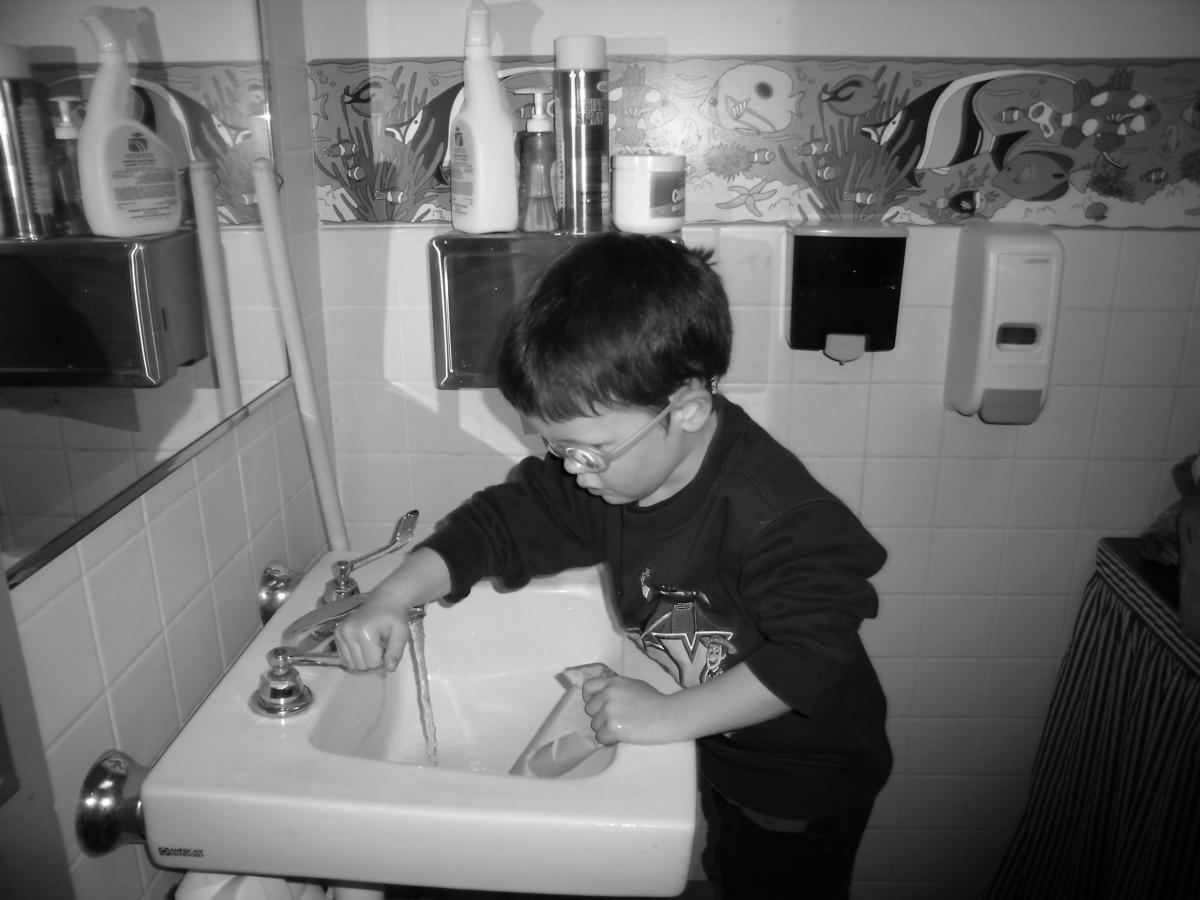 Young boy with glasses turns water on at sink