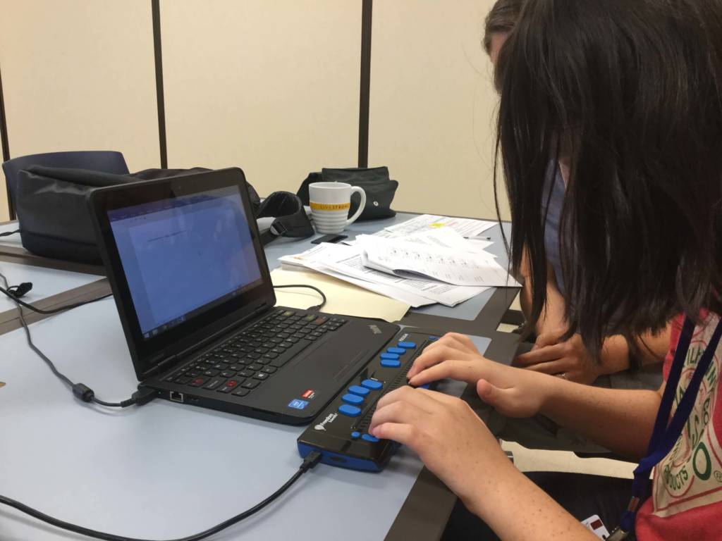 A girl uses a refreshable braille display with a laptop computer.