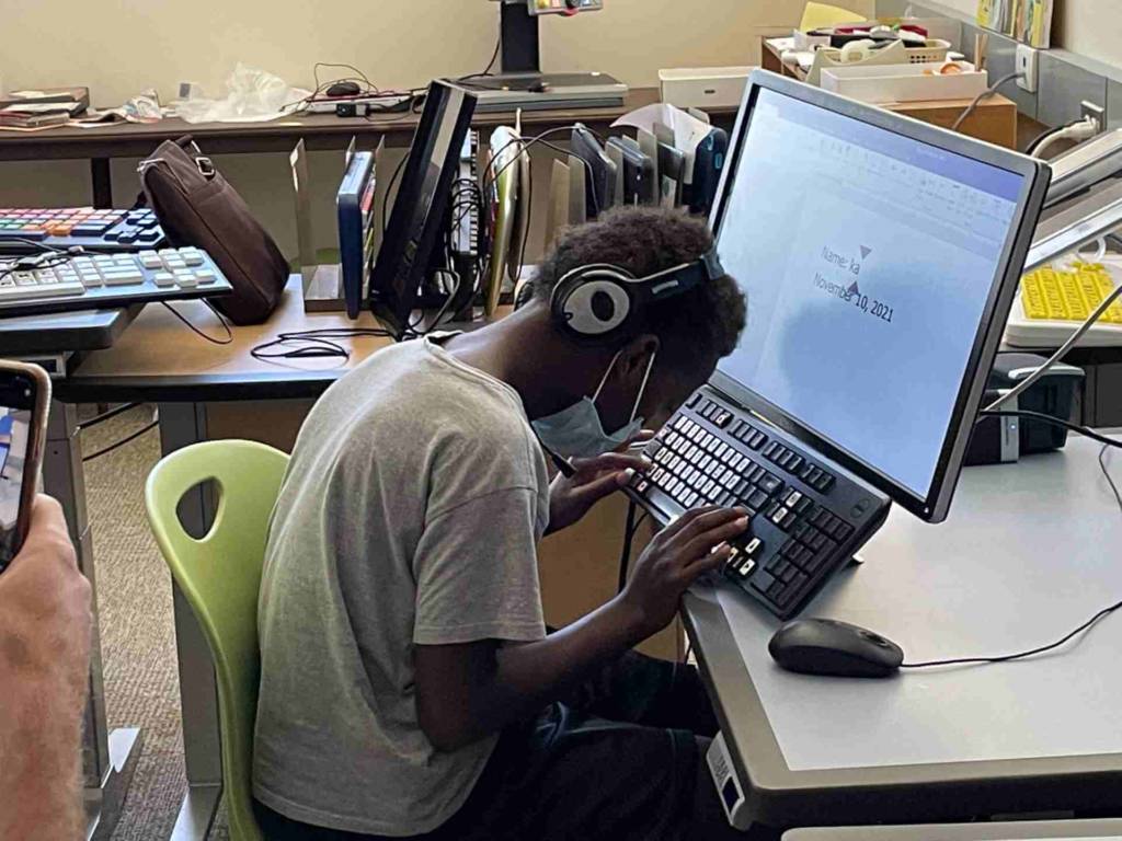  A boy with headphones uses a computer keyboard at a raised angle.