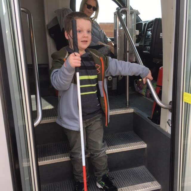 A young boy with a long cane stepping down from a bus