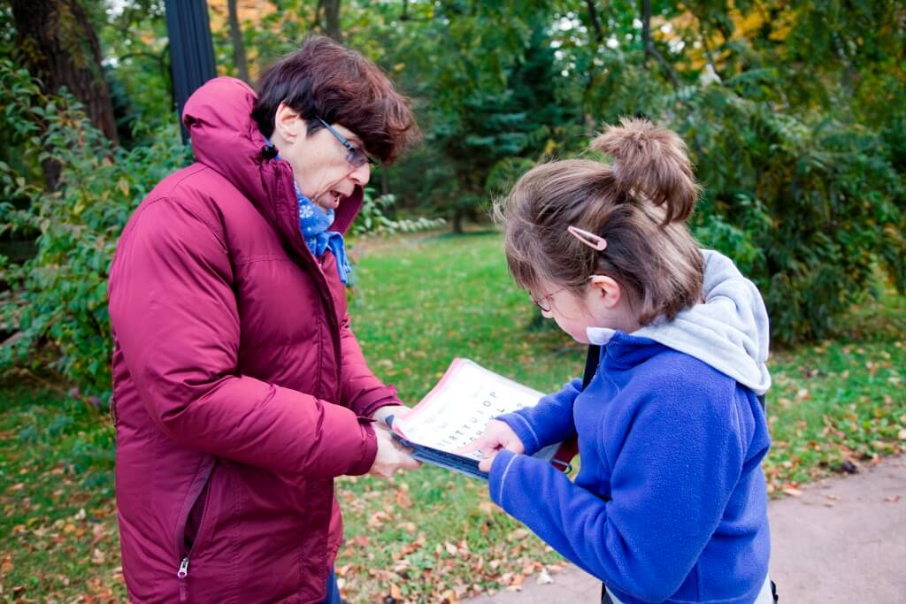 A girl points to a communication system outdoors with her teacher. 