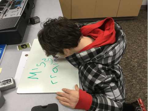A boy writes on a whiteboard with a green marker.