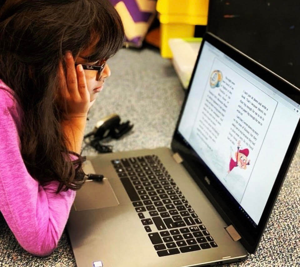 A girl with glasses reads text on a laptop computer.