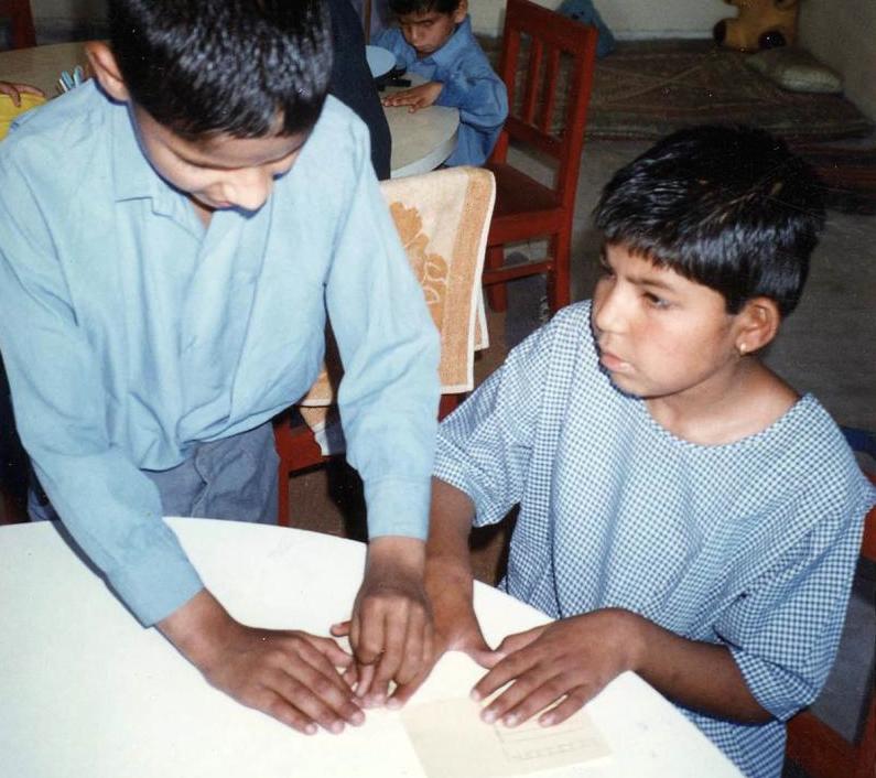 Two classmates in India read a braille postcard