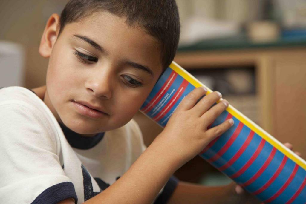 A young boy with his ear against a sound tube.