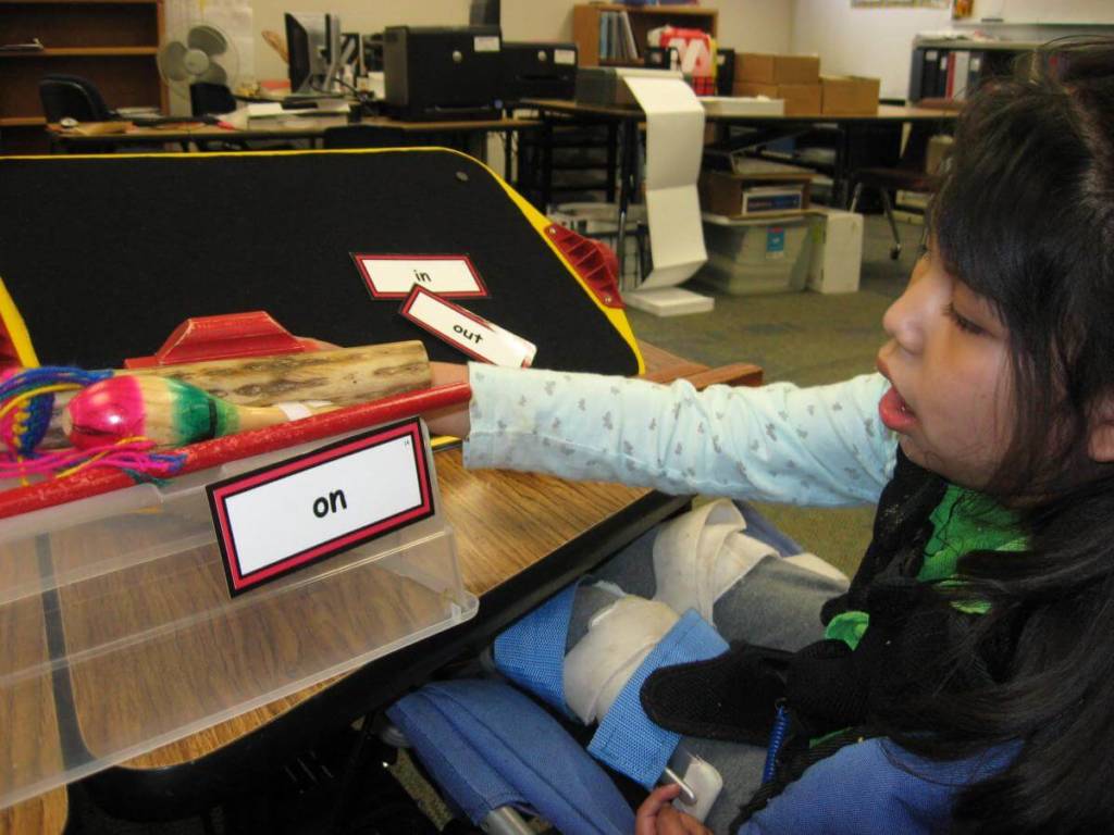  A girl in a wheelchair reaches towards a card with the word “on” printed on it.