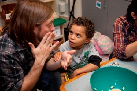 A young boy looks at his teacher’s face as his teacher signs to him.