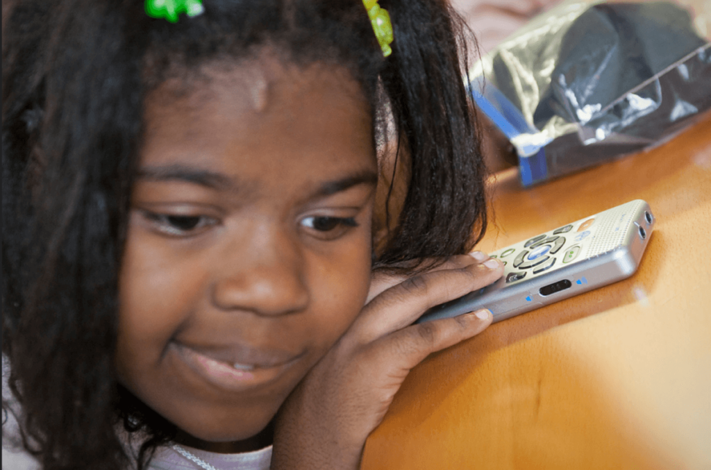 A young girl listens using an assistive technology device.