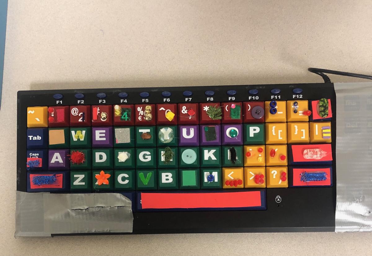 Sherry adapted the computer keyboard with textures. A computer keyboard has small textures velcroed to the keys. Other parts of the keyboard are covered with silver duct tape.