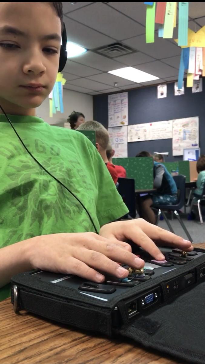 A student wearing headphones uses a BrailleNote adapted with textures on each key.