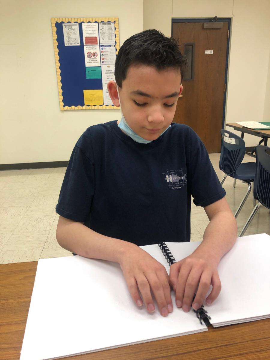 A student uses both hands together to read a story written in contracted braille.