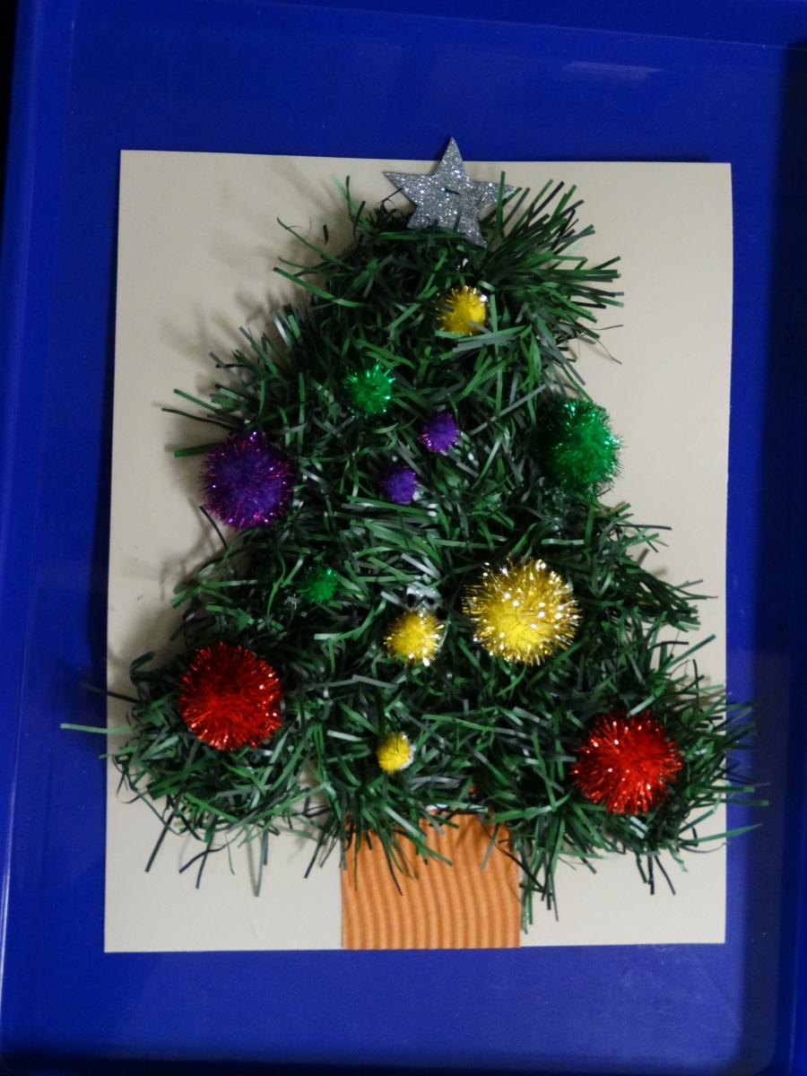 garland formed into a tree on a piece of blue paper with pom poms and stickers