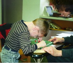 A boy bends over the desk in a cramped position, leading to chronic neck and back pain.