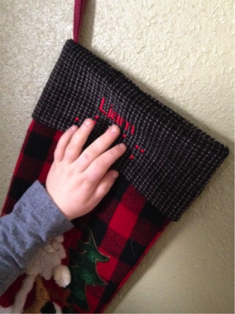 A young boy's hand reads the braille on a Christmas stocking.