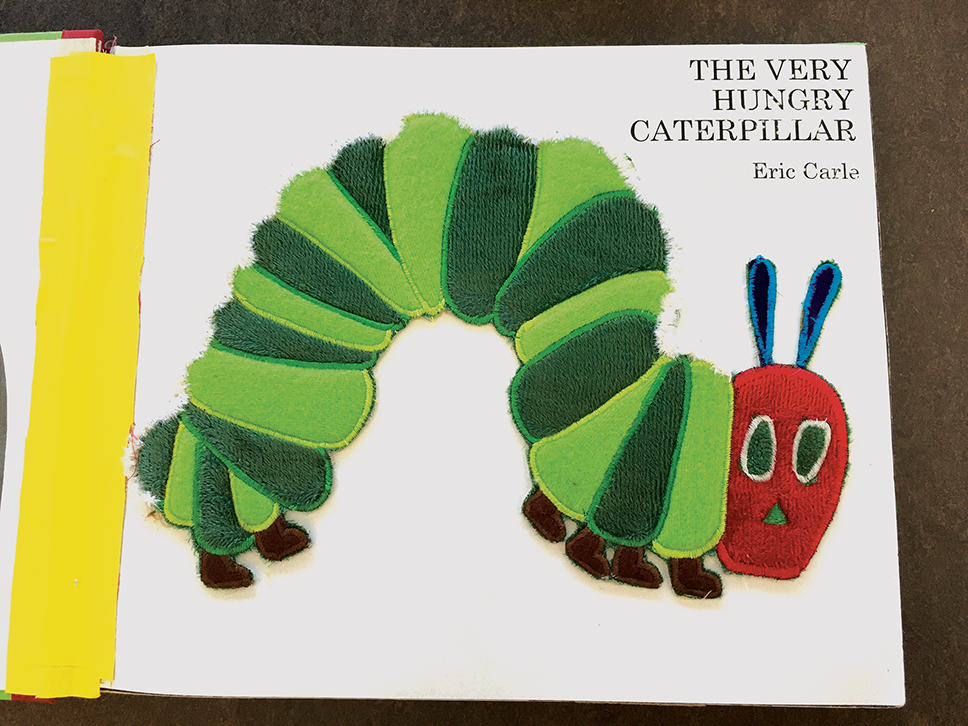 Picture of the title page of The Very Hungry Caterpillar. It has a colorful tactile image of a caterpillar, and the title is written in braille.