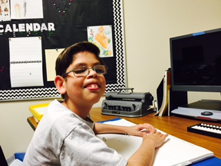 A boy with a braille book smiles at the camera