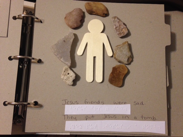Wooden figure surrounded by small stones with text in print and braille