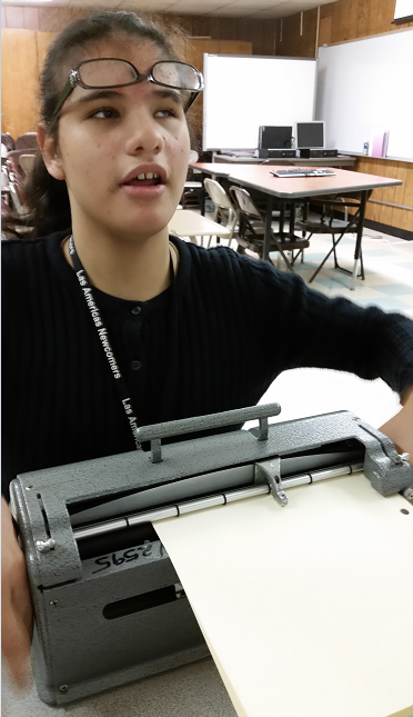 Heba, a young woman with glasses on her forehead, types on a brailler.