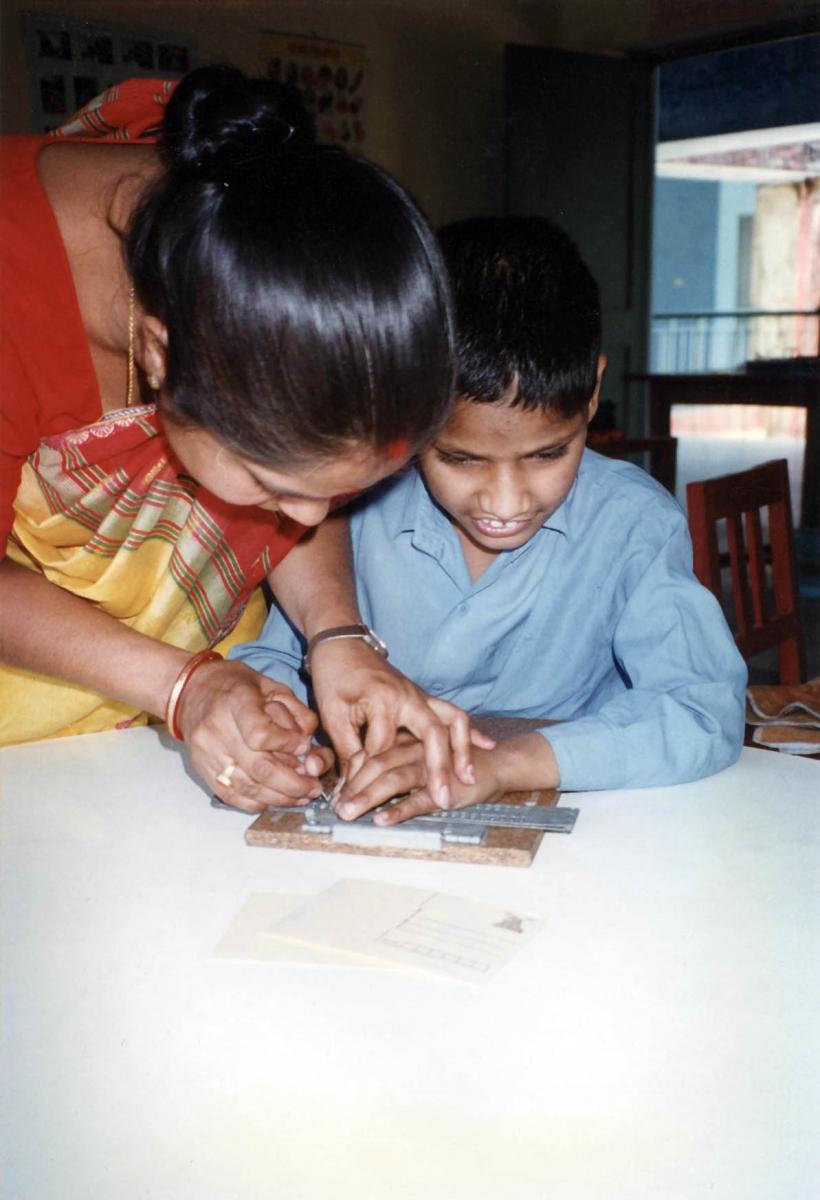 Tilak learns to write braille with a slate and stylus with his teacher.