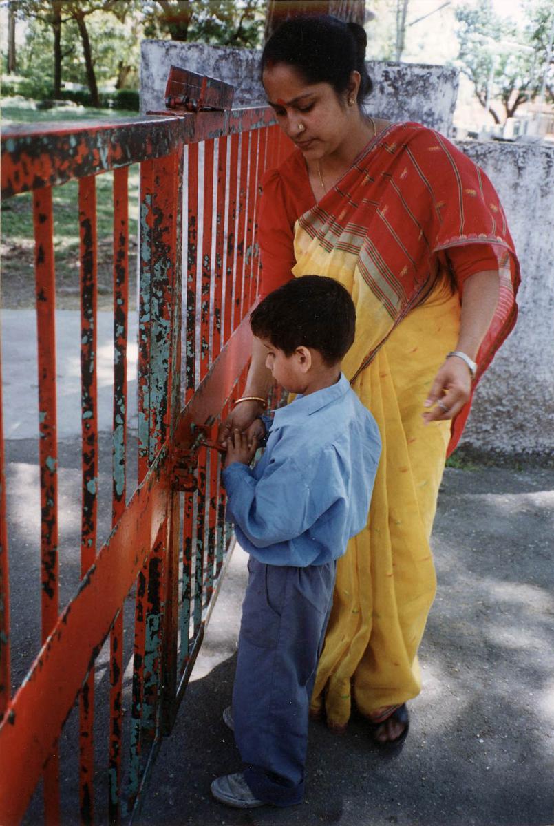 A young boy places the key in the lock to the school gate.