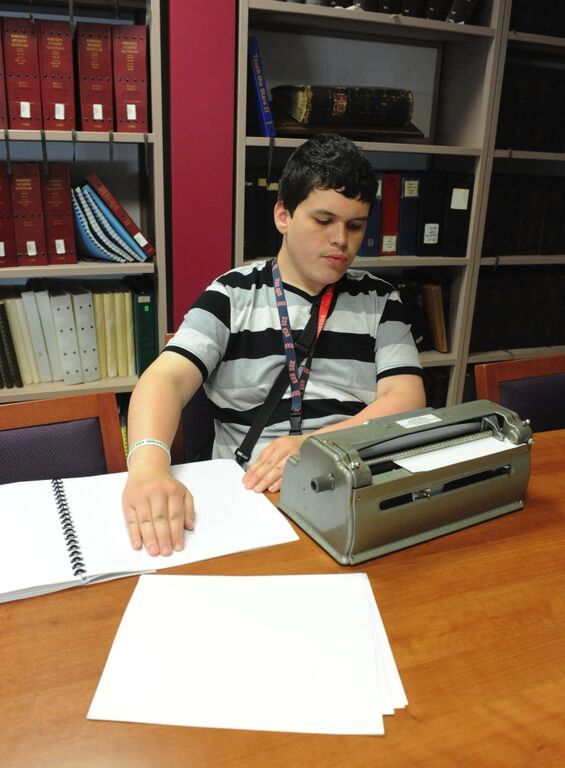 student in black and white striped shirt using braille writer
