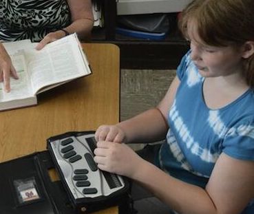 student in blue shirt using braille notetaker