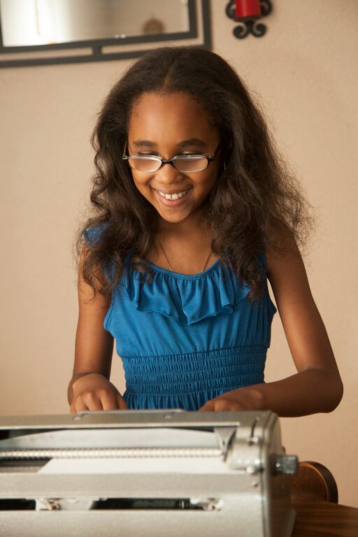 girl with glasses in blue dress using brailler