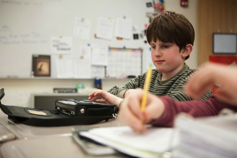 student in green striped sweater using braille writer