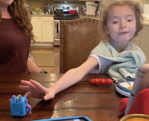 A child looks away while reaching after first visually regarding a bright blue fidget toy in her right visual field.