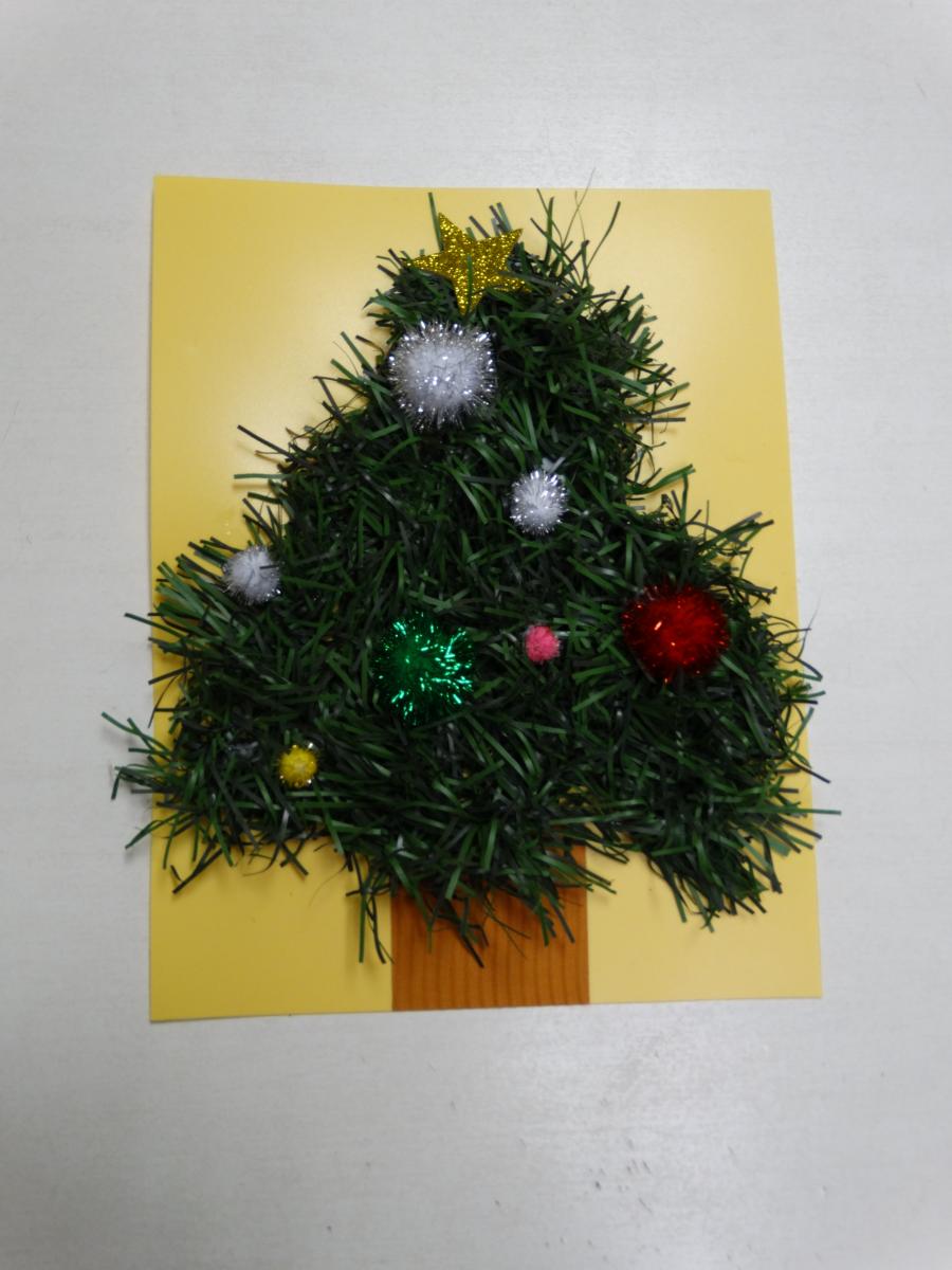 garland formed into a tree on a piece of yellow paper with pom poms and stickers