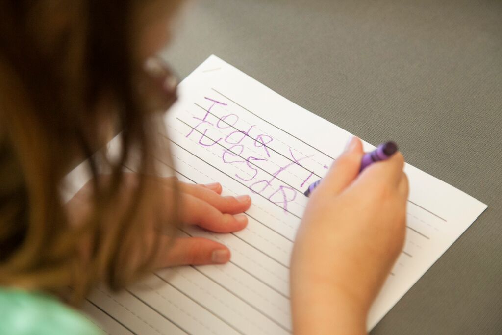 Student writing with purple crayon on lined paper