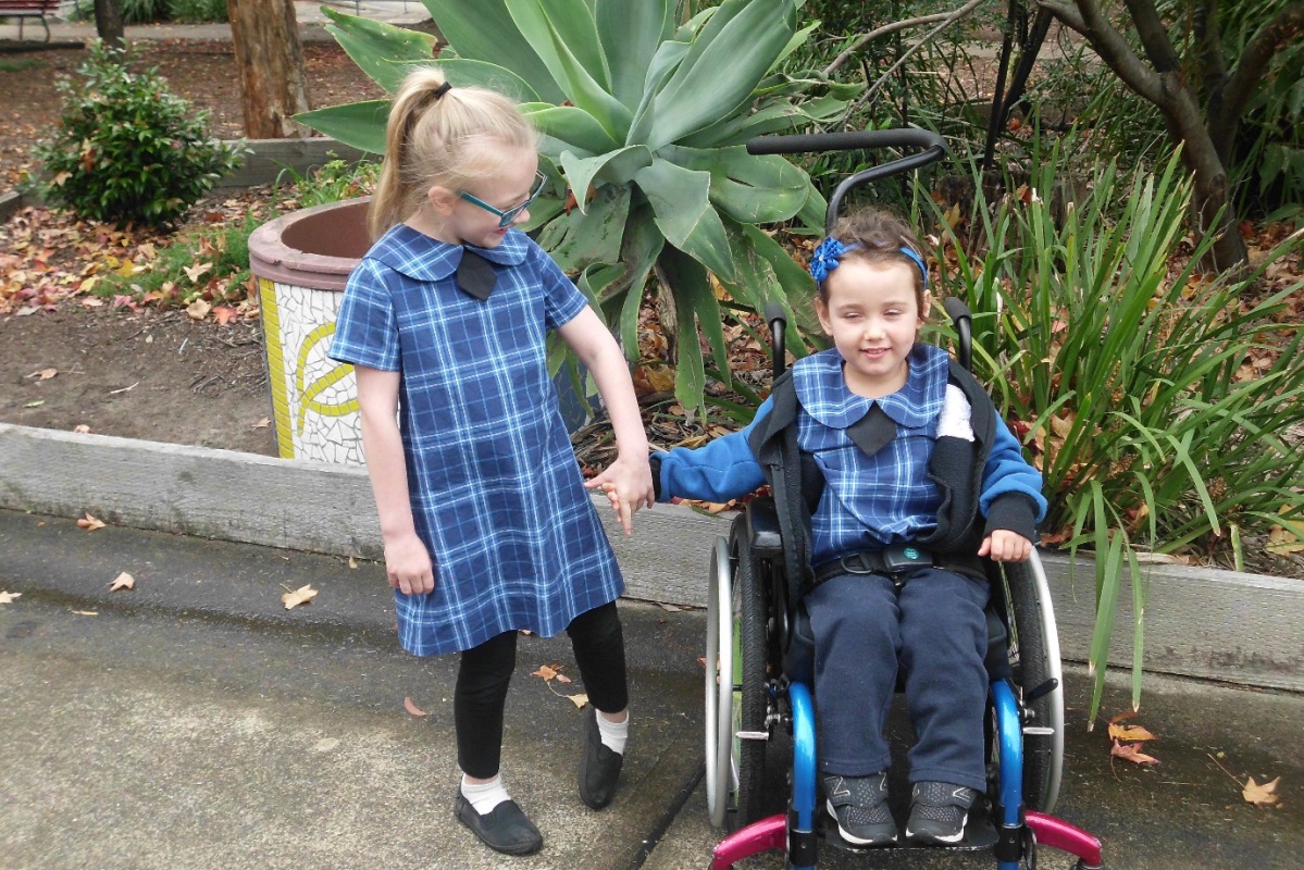 Sarah and Chloe, two young girls in blue dresses holding hands, one of them is in a wheelchair