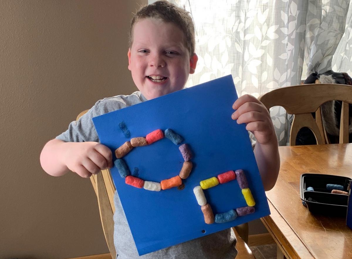 A boy who is deafblind holds up his Magic Nuudles design.