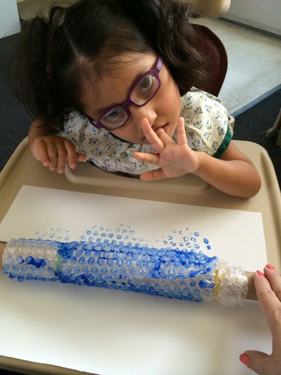 A young girl makes a painting with bubble wrap and a rolling pin.