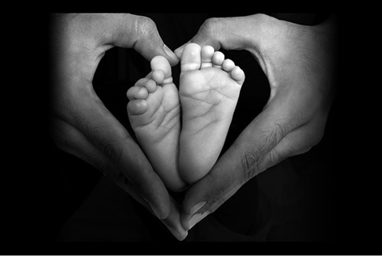 Baby feet with adult hands forming a heart shape around them