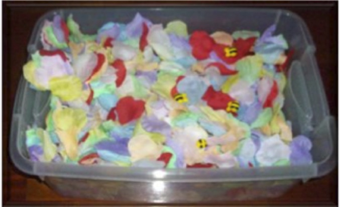 Sensory bin filled with artificial, silk flower petals and plastic bees to find