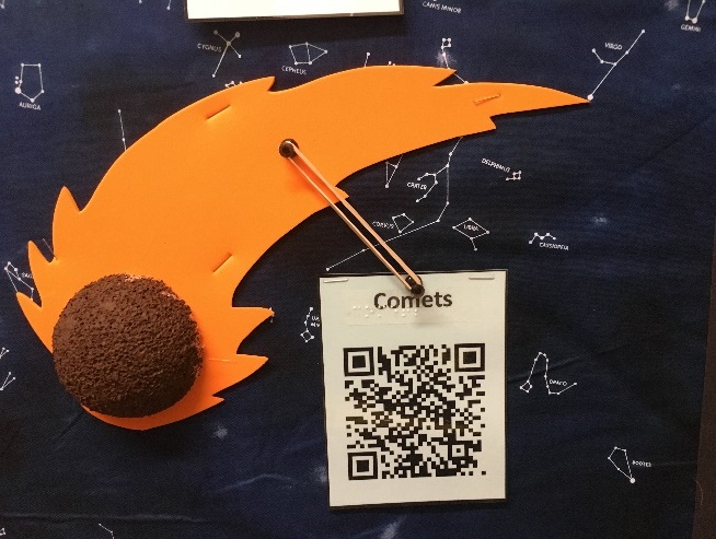 tactile portrayal of a comet on a bulletin board labeled with a QR code, braille,and print
