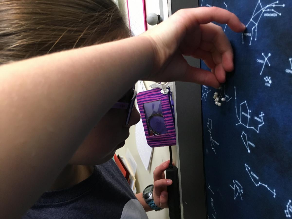a girl putting in a pin in the bulletin board to mark a star constellation