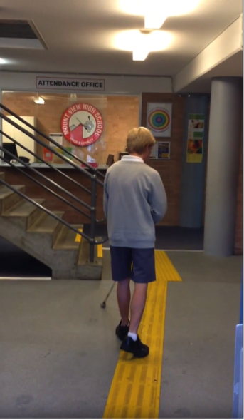 A photograph shows a teenage boy in school uniform using his cane and walking along a tactile pathway towards the Attendance Office. 