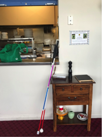 A photograph shows 2 long canes resting outside a service window in a bistro. Through the window a small section of a restaurant kitchen can be seen. 